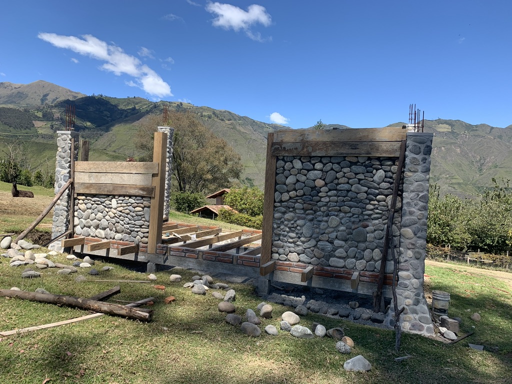 River-stone walls under construction beneath a clear blue sky