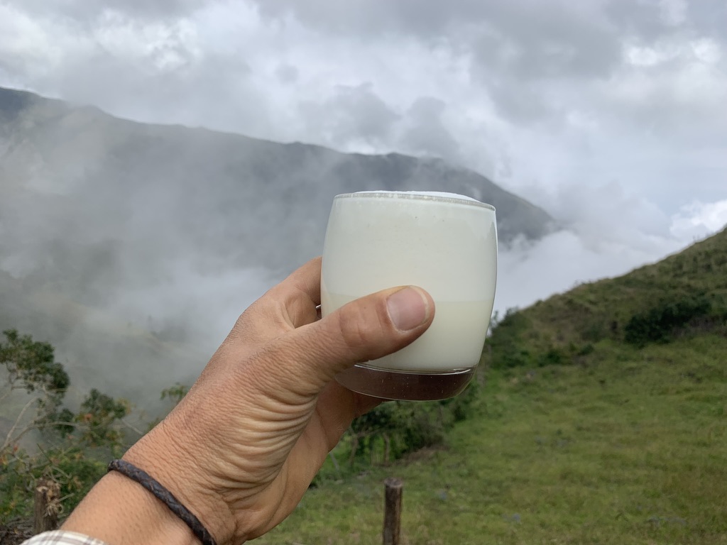 A glass of fresh milk held up against the cloud-wrapped mountains