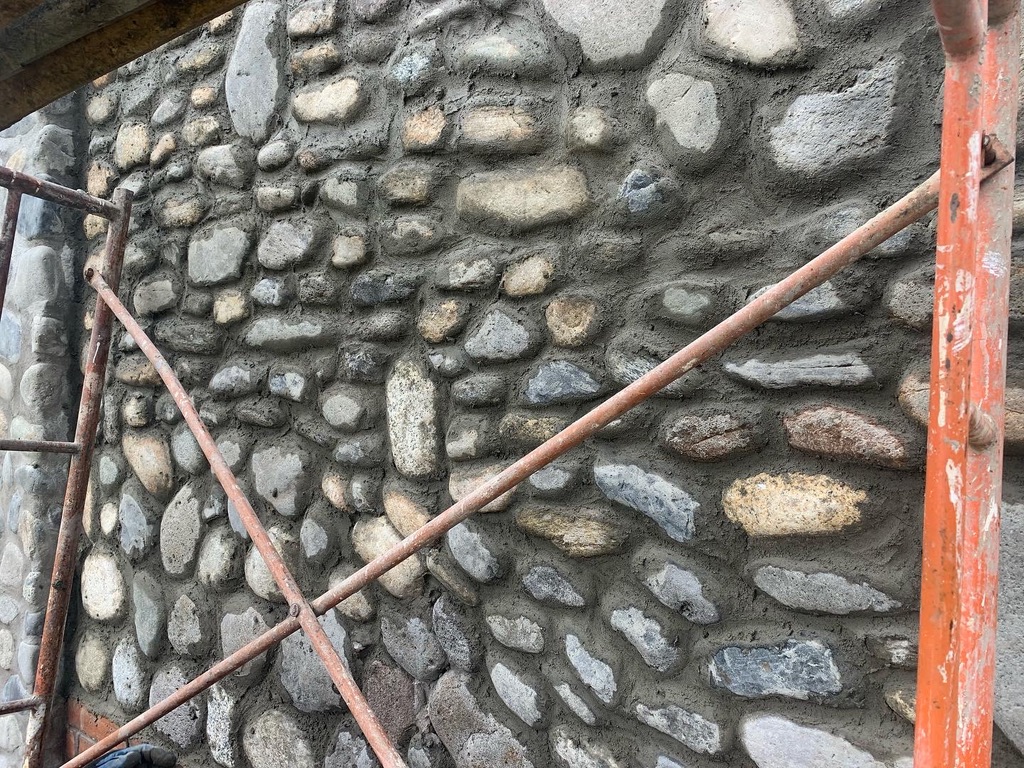 Close detail of river stones set in fresh mortar behind orange scaffolding
