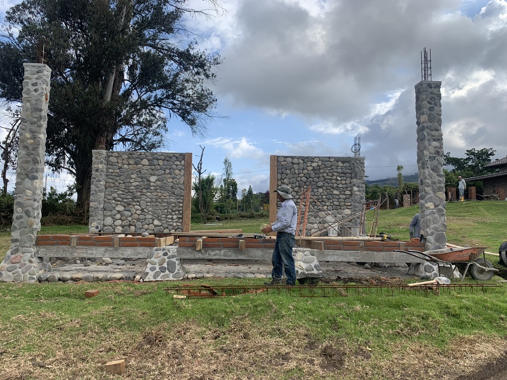 A mason working on river-stone wall panels between tall stone columns