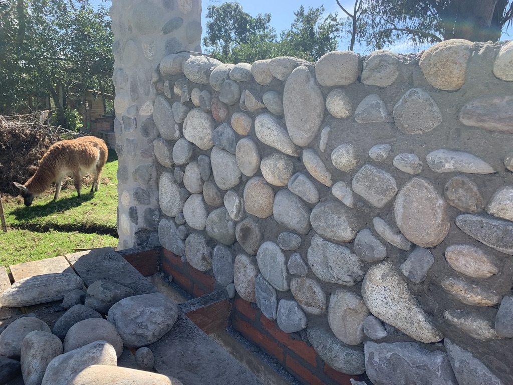 Close-up of a hand-laid river-stone wall with a llama grazing in the field