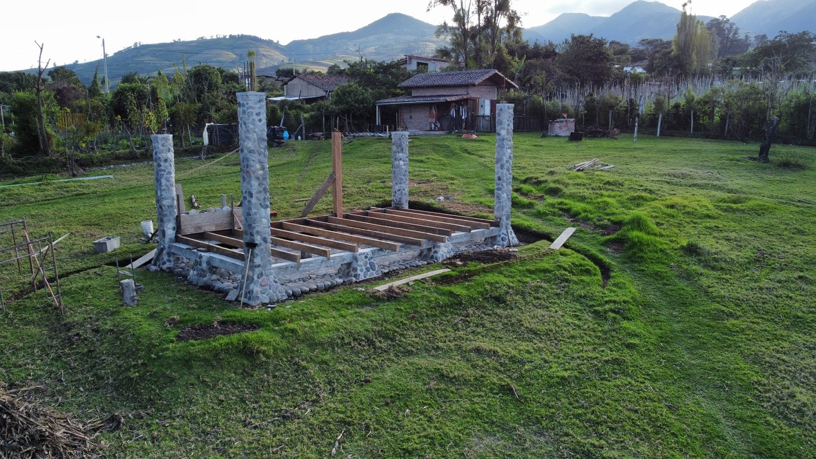 River-stone columns and floor joists under construction at dusk with mountains behind