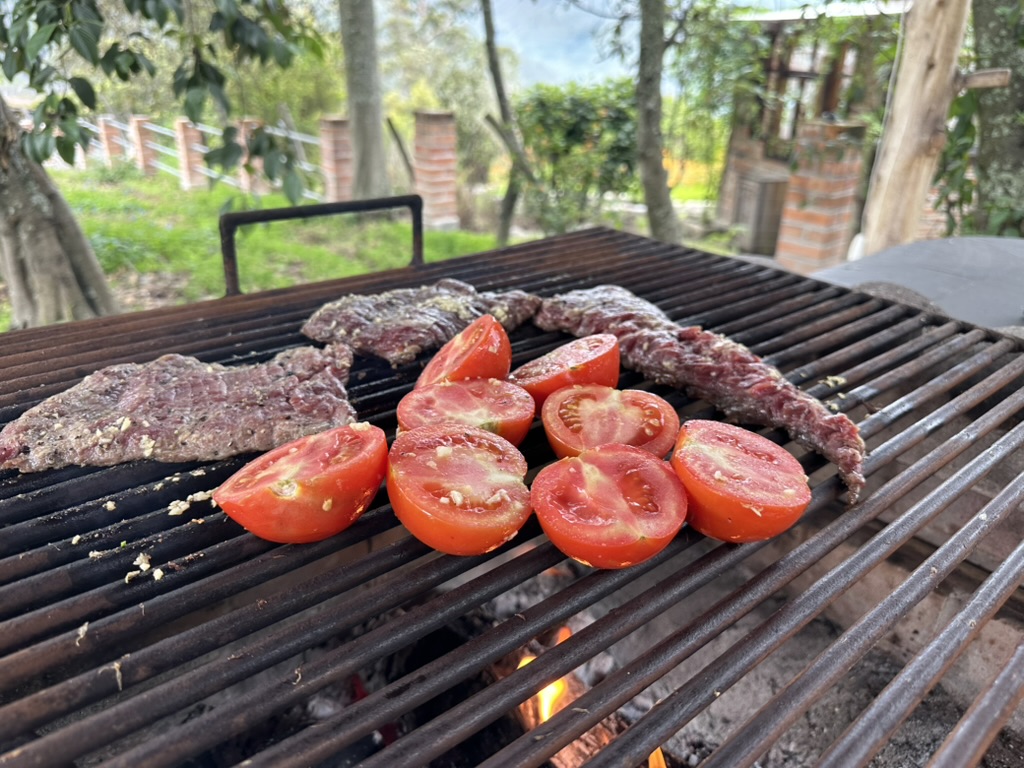 Steak and halved tomatoes over a wood fire on the farm grill